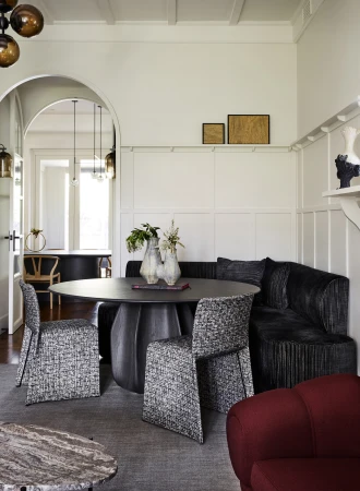 Interior view of a stylish dining room with a round table, upholstered chairs, and a built-in corner bench under framed artwork.