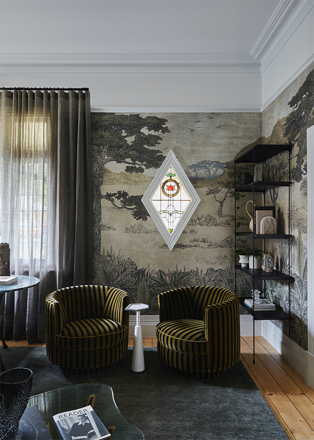 Living room interior with patterned wallpaper, green striped armchairs, a stained-glass window, and dark grey rug and curtains.