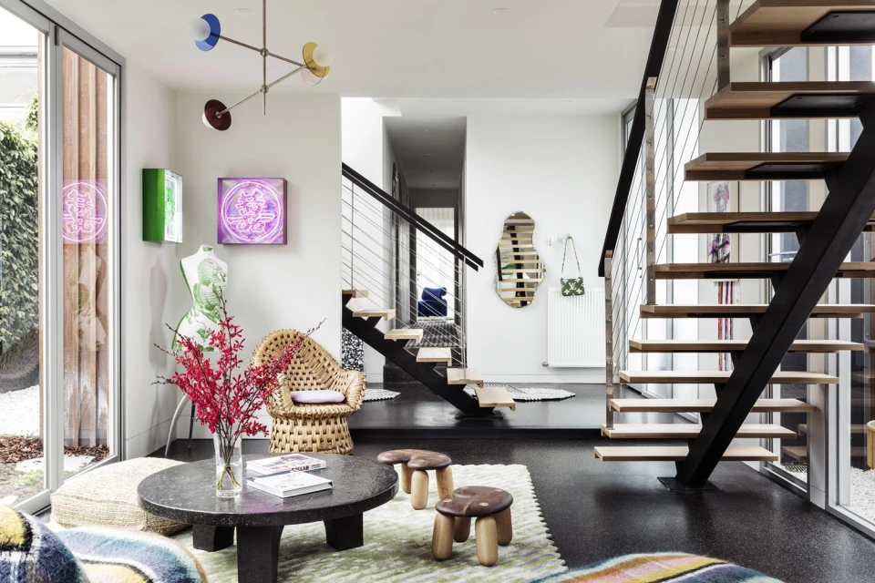 Eclectic interior design of a home living room featuring a woven chair, round coffee table, and floating stairs, creating a modern aesthetic.