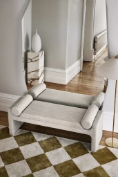 Upholstered cream bench sits on a green and cream checkered rug in a bright interior styled by Simone Haag.