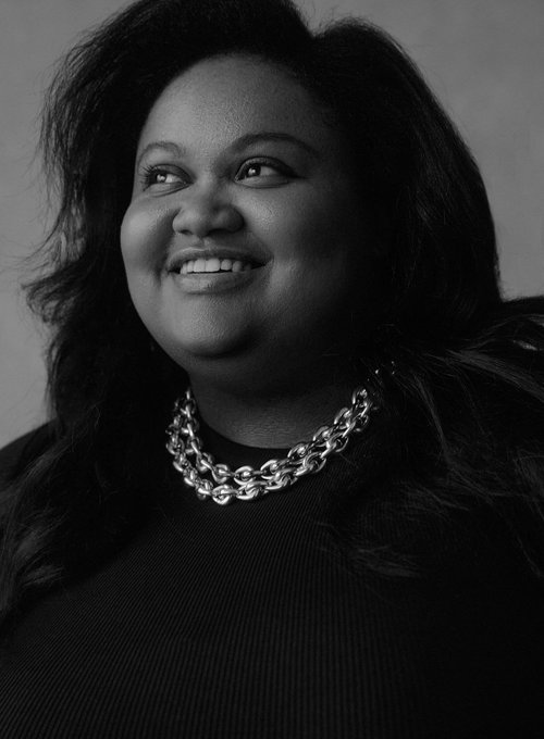 Close-up portrait of a smiling adult woman with dark hair wearing a double-strand silver chain necklace against a neutral background.