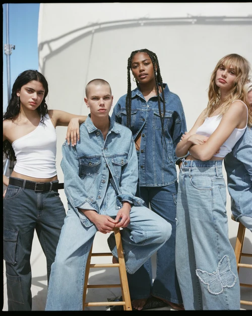 Four young adults showcase denim and white tops in a bright studio, embodying a modern, casual fashion aesthetic with a clean backdrop.