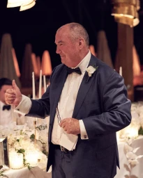 Man in a dark suit with a bow tie giving a thumbs up at a candlelit table setting