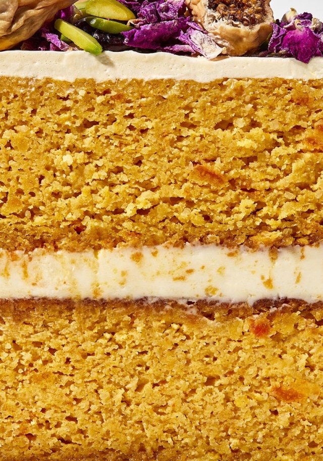 Close-up cross-section of a multi-layered cake featuring golden sponge layers, cream filling, topping with nuts and floral decorations.