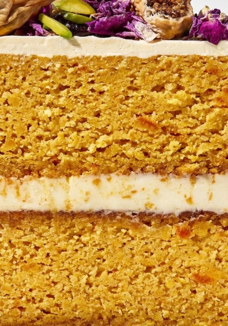 Close-up cross-section of a multi-layered cake featuring golden sponge layers, cream filling, topping with nuts and floral decorations.