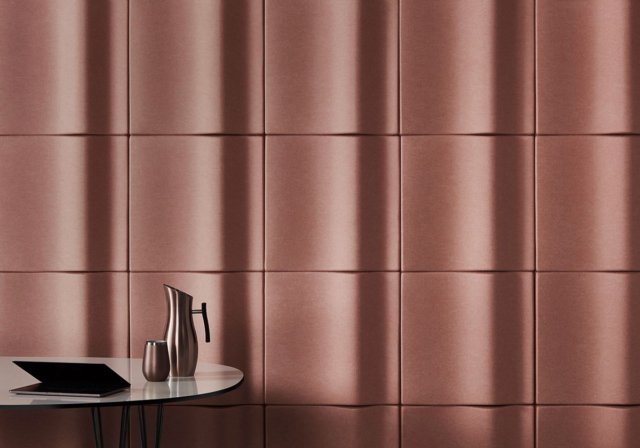 Interior design with a metallic pitcher and glass on a round table against a textured panel wall with geometric patterns and linear lighting.