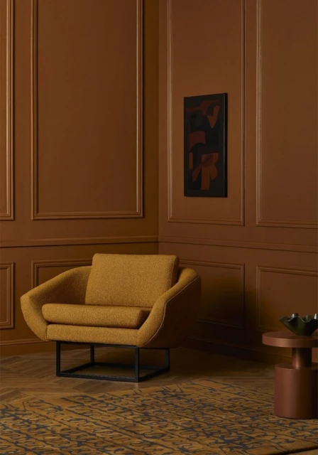 Interior with mustard-colored chair and abstract art on a sienna-toned wall. Wood flooring and warm, inviting lighting.