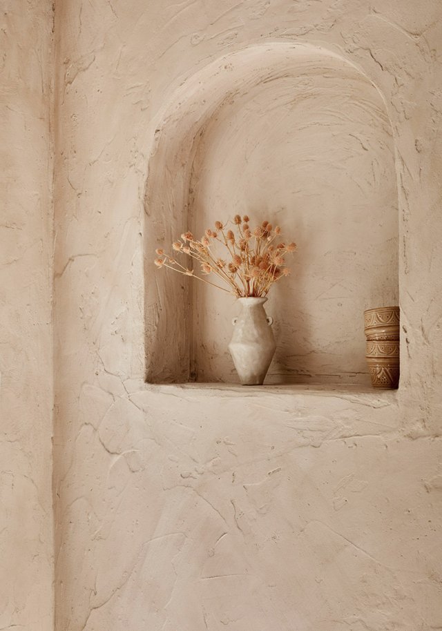 Still life of dried floral arrangement in a vase set inside a decorative wall niche; beige color palette.