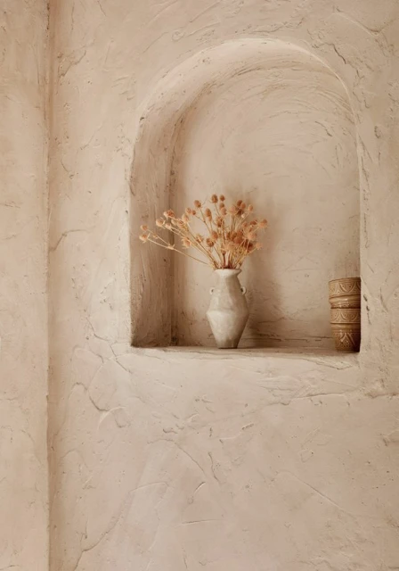 Still life of dried floral arrangement in a vase set inside a decorative wall niche; beige color palette.