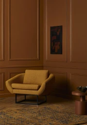 Mustard yellow textured armchair in a monochromatic brown paneled room with a small side table and patterned rug