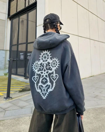 Back view of a person with braided hair wearing a black hoodie with a white graphic design, black hat, and wide-leg olive-green pants outdoors.