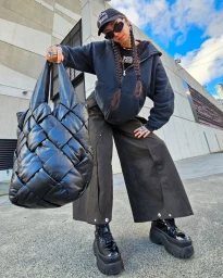 Woman wearing dark zip hoodie and wide trousers holding a large black woven leather handbag outdoors in Sydney
