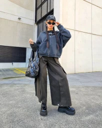 Content creator Tara Chandra wearing a dark zip hoodie, wide cargo pants, and platform shoes against an urban building exterior.