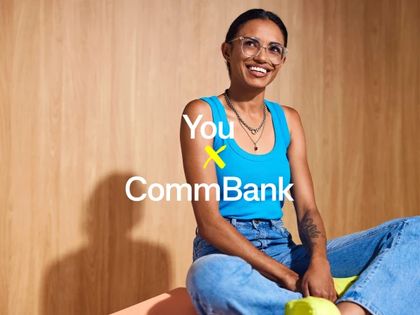 Smiling woman wearing clear glasses and a blue tank top sitting against a light wood paneled wall.