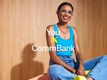 Smiling woman wearing clear glasses and a blue tank top sitting against a light wood paneled wall.