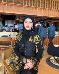A woman wearing a black hijab and ornate gold and black patterned cape seated inside a restaurant.