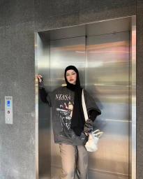 Content creator Tuba Dagli in Sydney posing inside an elevator wearing a black hijab and graphic t shirt