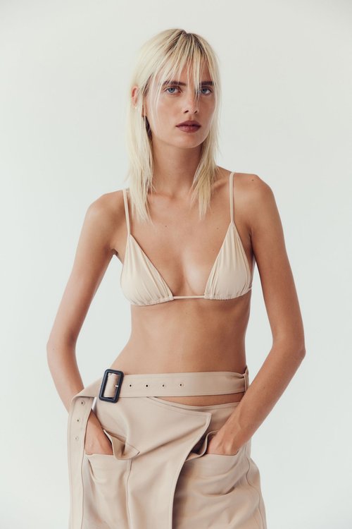 Fashion portrait of a fair-skinned woman with blonde hair wearing a beige bra top and matching wrap skirt, gazing at the camera.