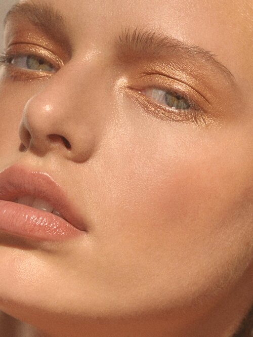 Close-up of a woman's face with golden eyeshadow and glossy lips, showcasing beauty makeup in soft, natural light.