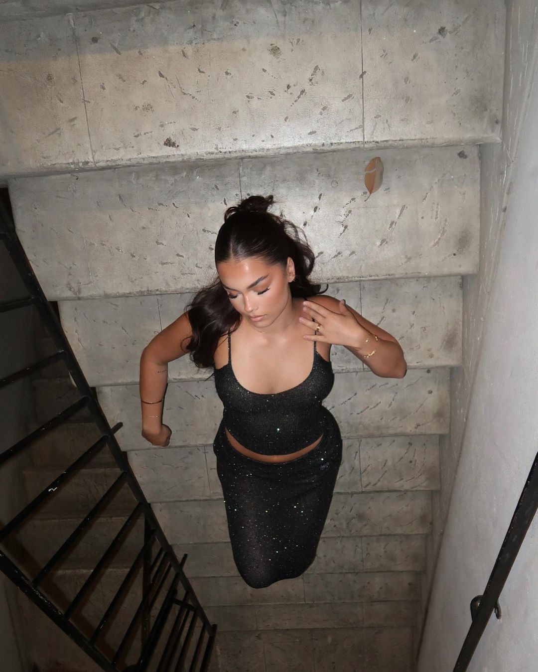 Woman in black sparkly dress stands on concrete stairs, viewed from above in a fashion style portrait, with a shallow depth of field.