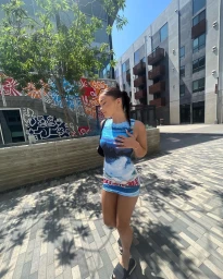 Woman in blue printed dress standing outdoors on paved public square by modern buildings