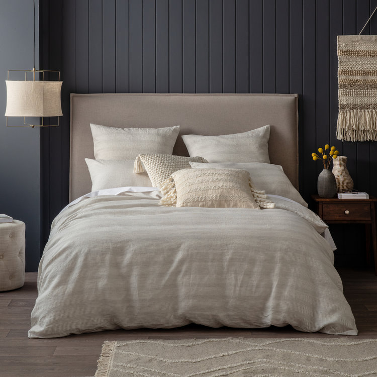 Bedroom interior with a neatly made bed featuring a neutral-toned duvet, decorative pillows, wooden nightstand, and hanging lamp.