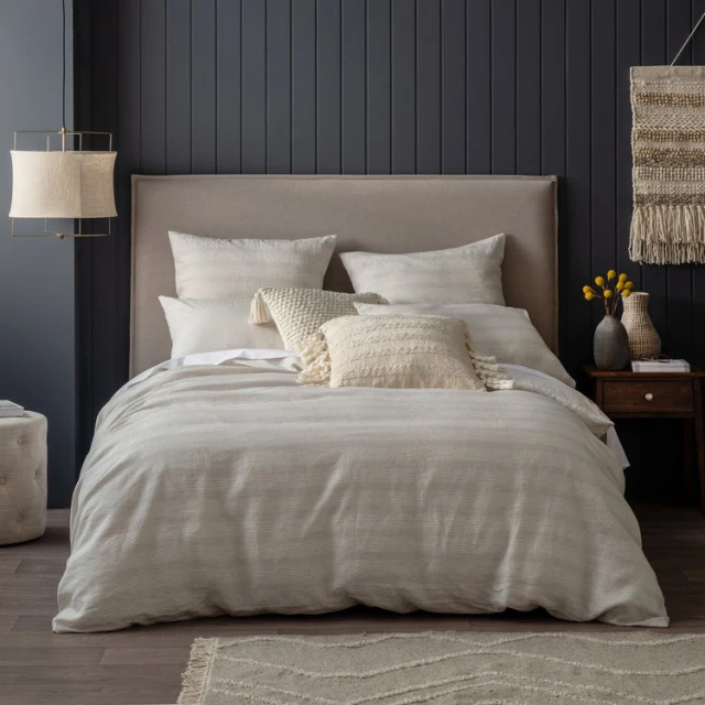 Bedroom interior with a neatly made bed featuring a neutral-toned duvet, decorative pillows, wooden nightstand, and hanging lamp.
