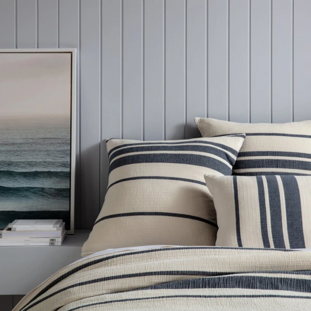 Bedroom interior with striped pillows and duvet cover on a bed, complemented by a framed ocean picture on the wall.
