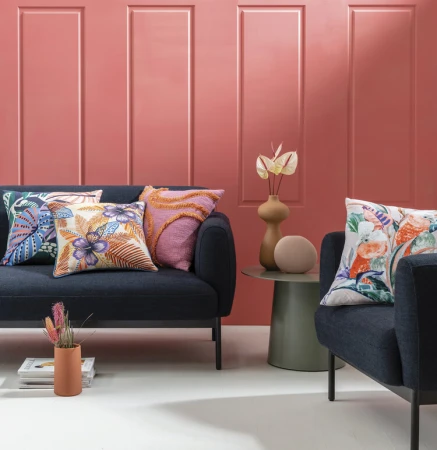 Indoor living room scene with a dark blue sofa adorned with patterned cushions, complemented by flower vases and a salmon-colored wall.