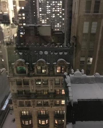 High-angle night view looking out over historic urban buildings covered in fresh snow with illuminated windows.