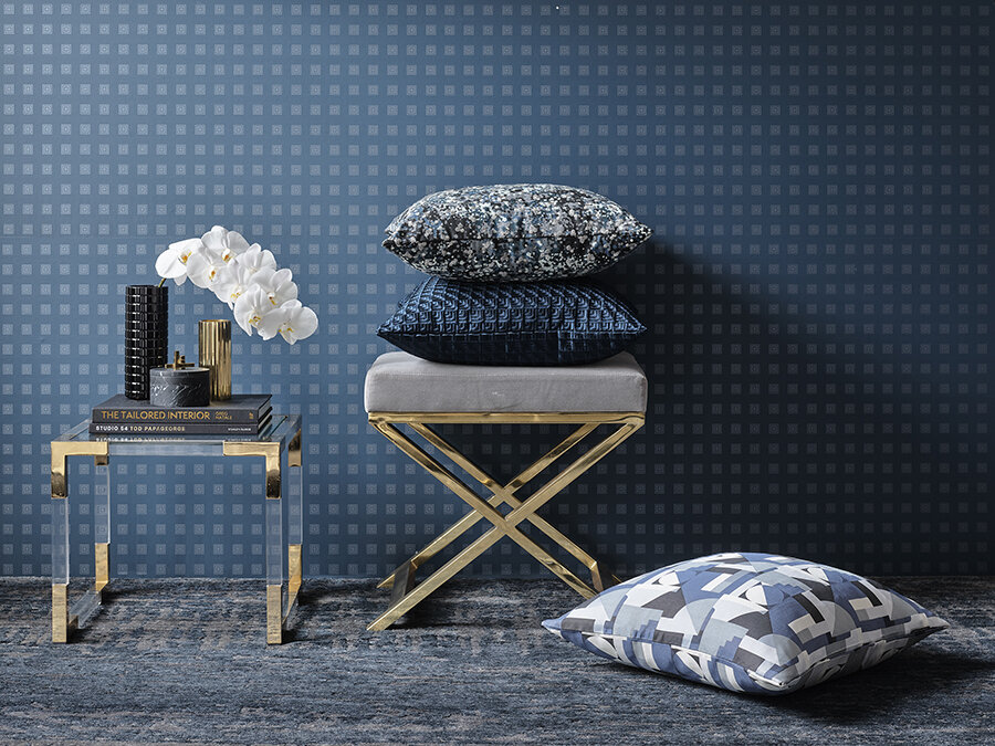 Interior design featuring a stack of cushions on a gray bench with gold legs, complemented by a small table with a vase of flowers.