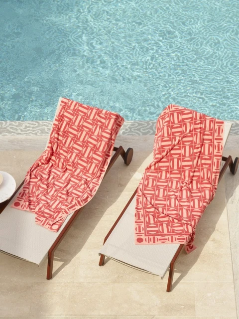 Two lounge chairs with coral patterned towels sit beside a pool with turquoise water, creating a summery and relaxing poolside scene.