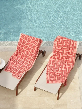 Two lounge chairs with coral patterned towels sit beside a pool with turquoise water, creating a summery and relaxing poolside scene.