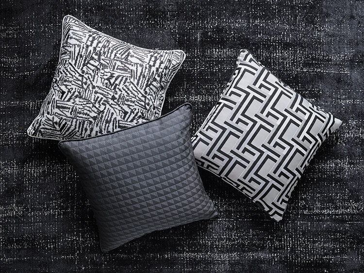 Three decorative pillows featuring geometric and abstract patterns are arranged on a black textured rug, creating a modern and stylish home decor scene.