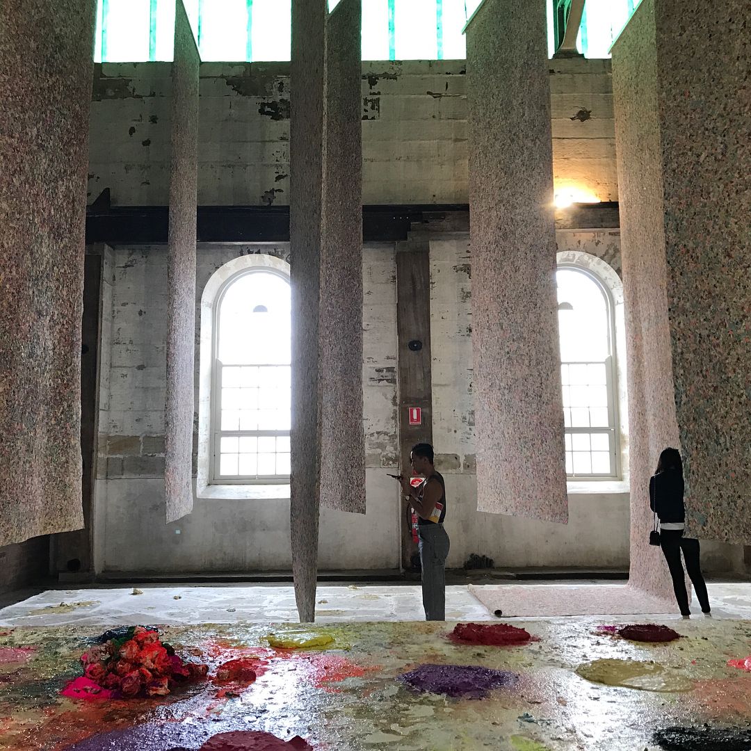 Interior of a building with installation art featuring suspended panels and colorful floor art, captured in a medium shot.