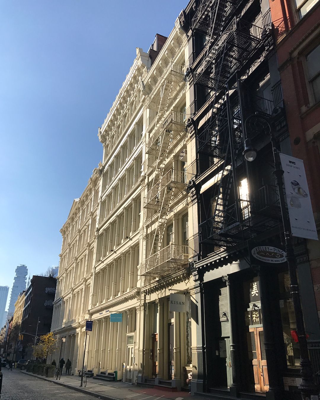 Urban street scene featuring tall historic buildings in contrasting colors, detailed architecture, and clear blue sky, creating a vibrant city view.