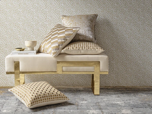 Interior still life featuring a beige and gold bench with patterned pillows, a decorative bowl, books, set against a patterned wallpaper.