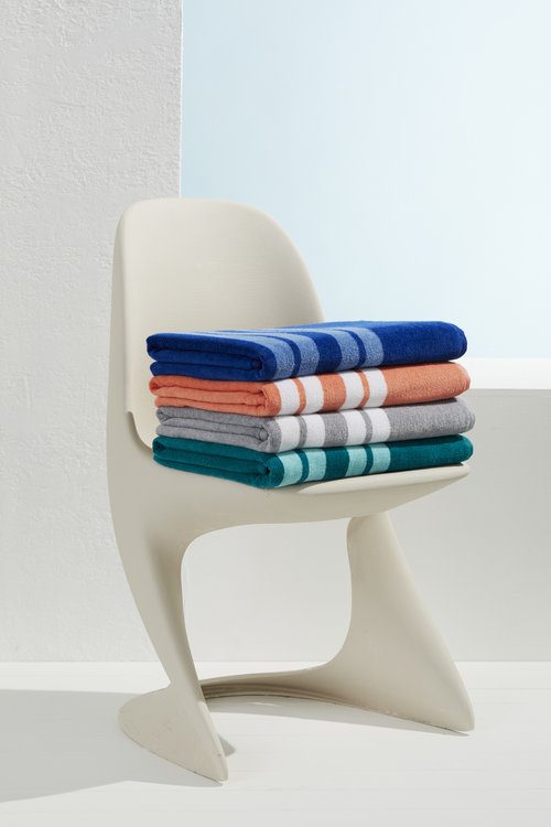 Stack of folded beach towels on a white modern chair in a bright studio. Colorful striped cotton towels, indoor, product shot.