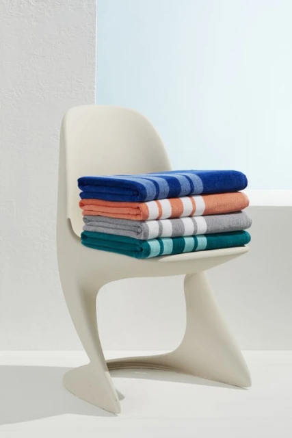 Stack of folded beach towels on a white modern chair in a bright studio. Colorful striped cotton towels, indoor, product shot.