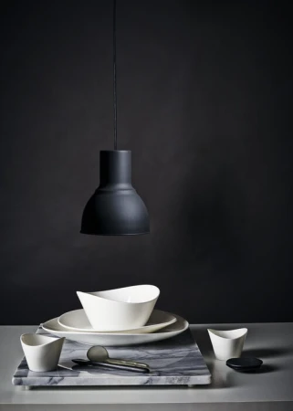 Still life photograph of white ceramic dishes and a gray marble cutting board under a modern black pendant lamp against a dark backdrop.