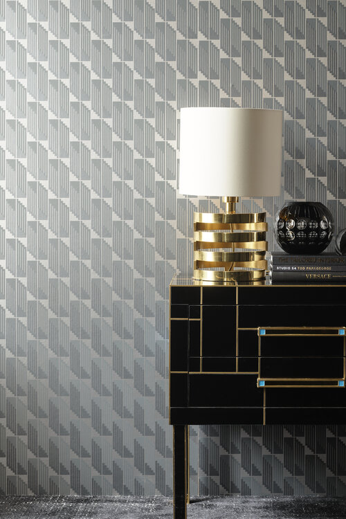 Interior decor featuring a gold table lamp, books, a black vase on a black cabinet with gold accents against a patterned wallpaper.