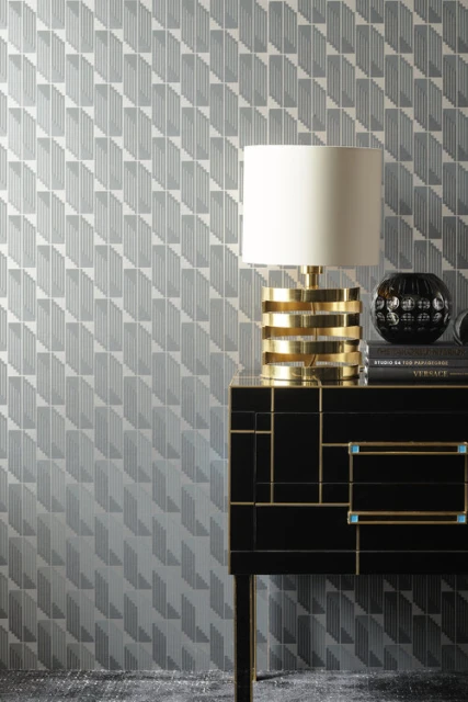 Interior decor featuring a gold table lamp, books, a black vase on a black cabinet with gold accents against a patterned wallpaper.