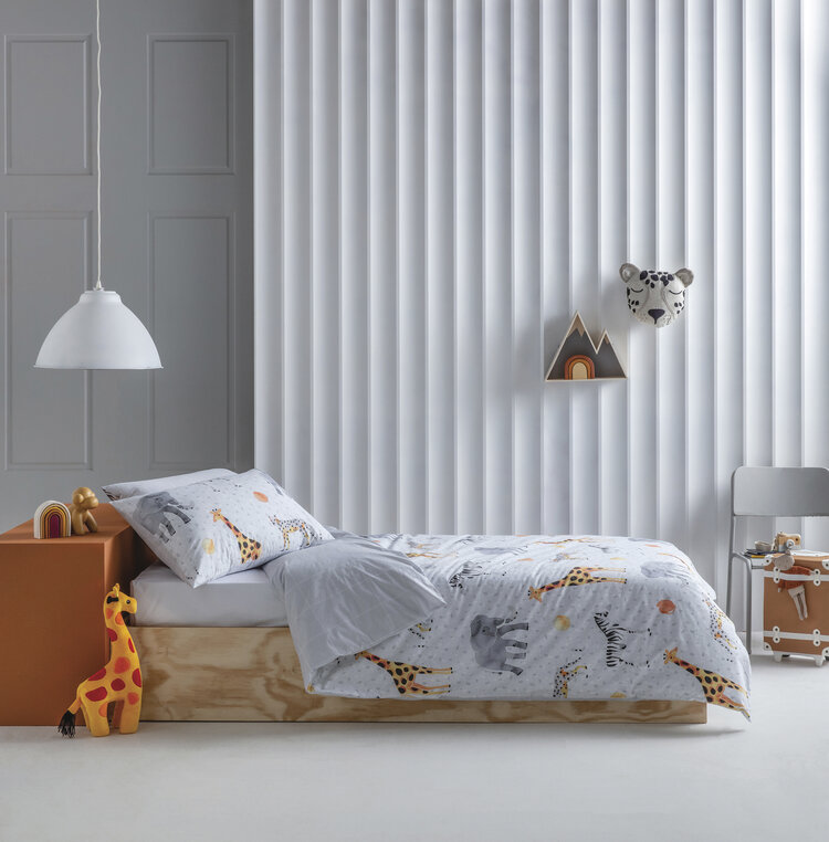 Child's bedroom featuring a twin bed with animal-themed bedding, wooden toys, white lamp, and a chair against a paneled wall.