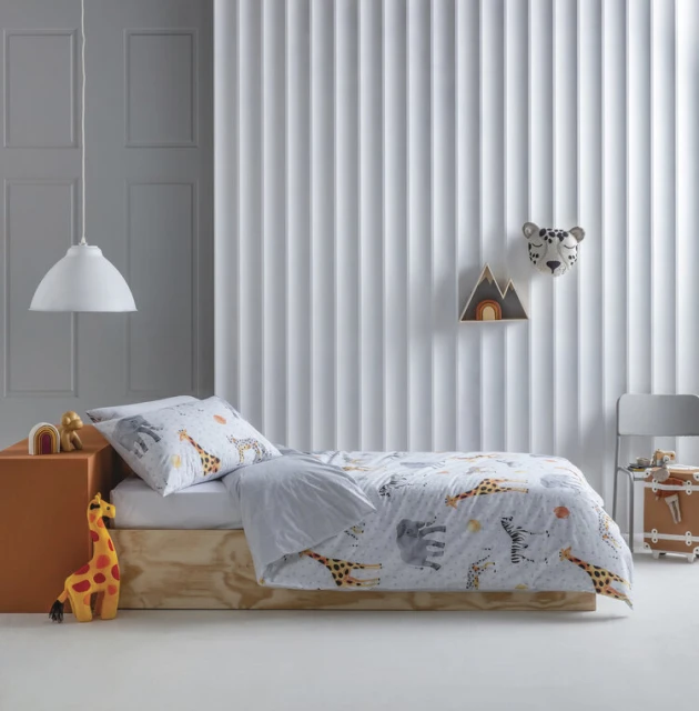 Child's bedroom featuring a twin bed with animal-themed bedding, wooden toys, white lamp, and a chair against a paneled wall.