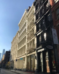 Exterior view of historic multi-story commercial buildings featuring ornate classical architecture and exterior fire escapes along a cobbled street.