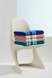 A stack of four colorful striped towels resting on a modern off-white plastic chair against a light neutral wall.
