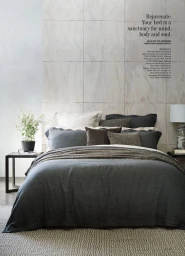 A neatly made bed styled with dark grey duvet, neutral pillows, and a throw blanket against a wood paneled wall.