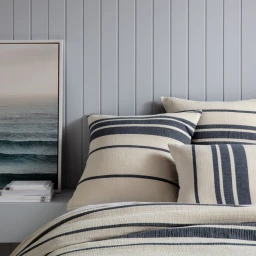 Close-up of a made bed styled with cream and dark blue striped cushions against light grey vertical panelling.