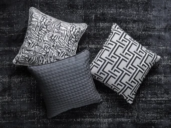 Three decorative cushions arranged on a dark textured rug viewed from above with geometric and abstract patterns.