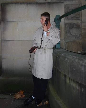 Man wearing beige trench coat holding a vintage corded telephone handset in Sydney, photographed by Will Stokoe.